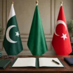 Editorial illustration of a treaty signing table with an open defence agreement folder, a fountain pen and reading glasses, backed by the standing national flags of Pakistan, Saudi Arabia and Turkiye.