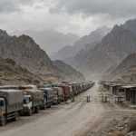 AI-generated editorial illustration of a long queue of idle cargo trucks waiting at a mountain border crossing with closed barriers and empty customs booths under an overcast sky.