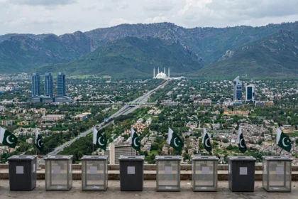 Empty ballot boxes with Pakistani flags overlooking the Islamabad skyline with the Faisal Mosque and Margalla Hills, as the ECP moves to schedule the capital's long-delayed local government elections